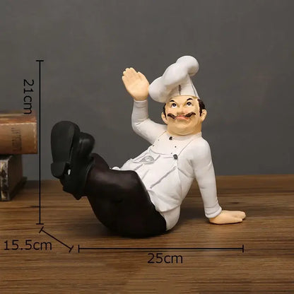 A cheerful white bearded chef resin figure in a white uniform and tall hat waving in a relaxed seated pose for kitchen decor