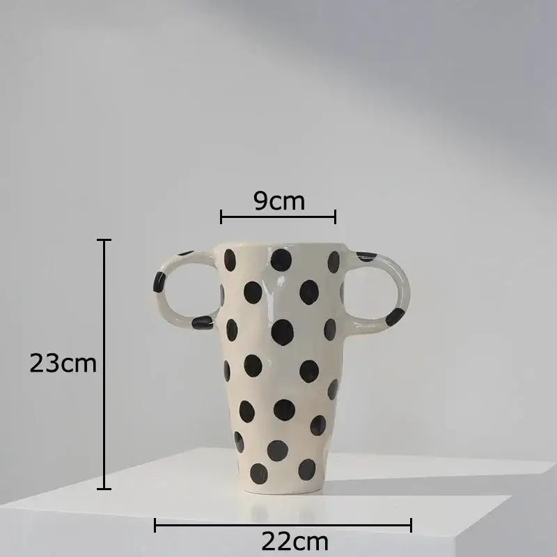 A tall cream-colored ceramic vase with black polka dot pattern and two looped handles for living room decor