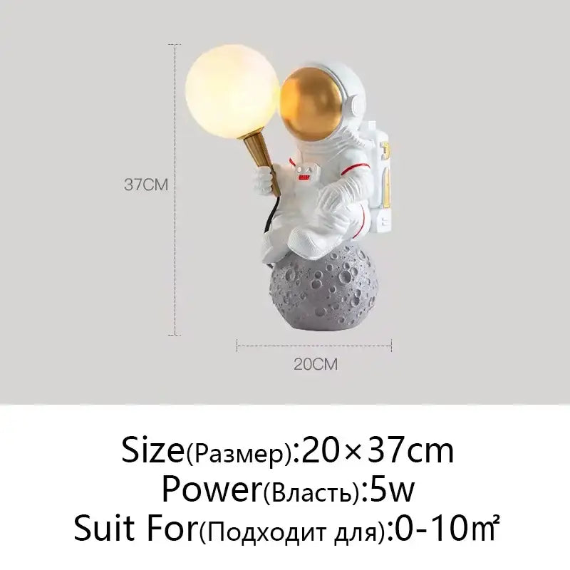 White and gold decorbites astronaut moon lamp with glowing sphere seated on gray textured moon planet table base