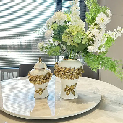 White and gold leaves ceramic flower vase with decorbites golden leaves embellishments holding white flowers and greenery
