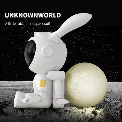 White and yellow galaxy bunny astronaut night light figurine with black visor sitting beside glowing moon lamp decorbites galaxy bunny