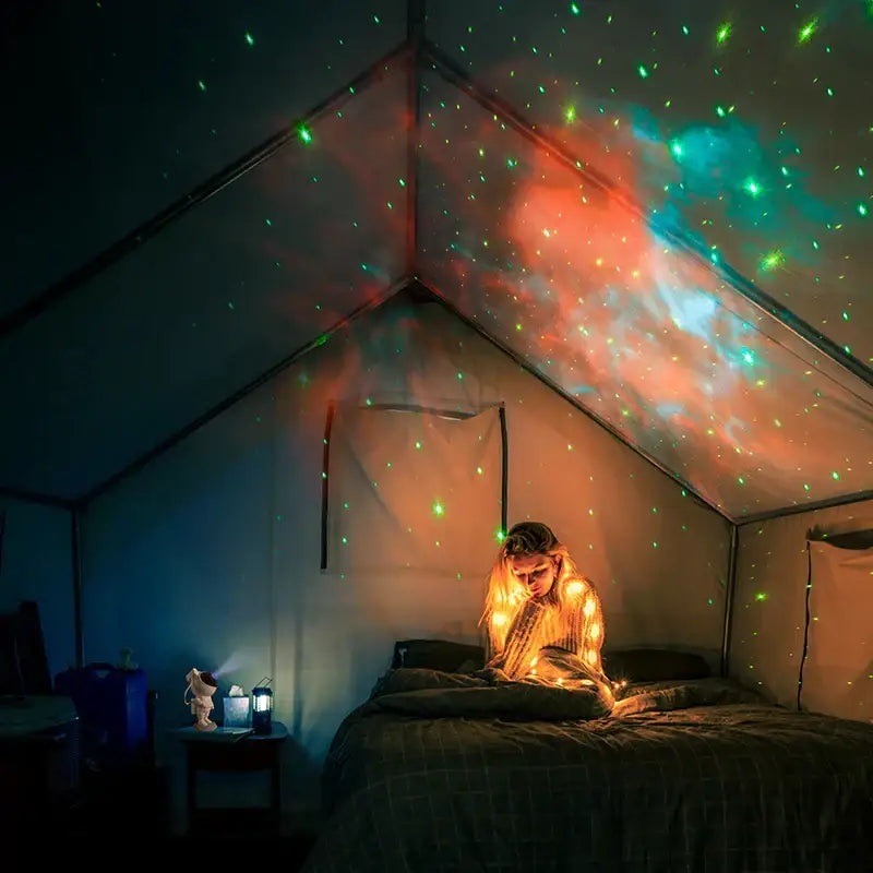 White astronaut star projector night light casting green and red cosmic patterns on tent ceiling for galaxy decor