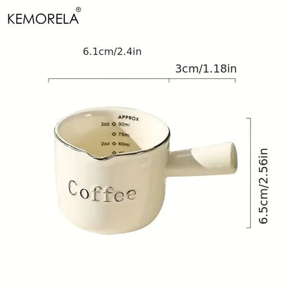 Cream-colored ceramic measuring cup with silver rim and handle featuring engraved coffee text and measurement markings