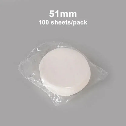 A stack of 51mm white circular disposable decorbites coffee filter papers in clear plastic packaging