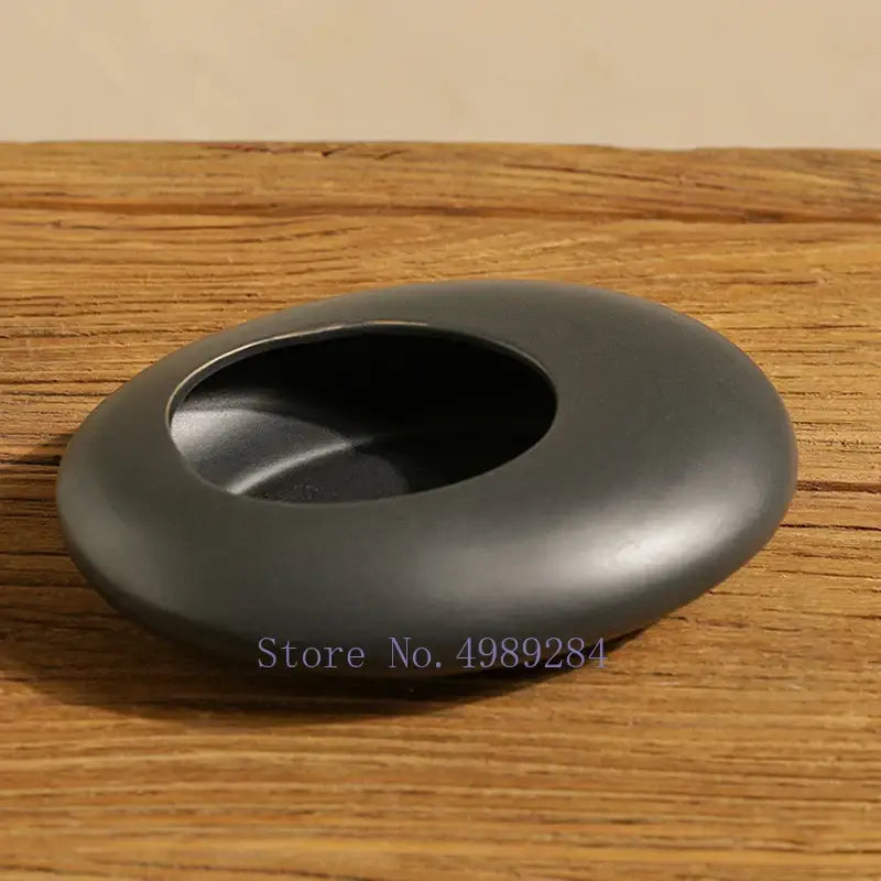 A smooth dark gray stone ashtray with a rounded oval shape featuring cobblestone deformation ceramic design