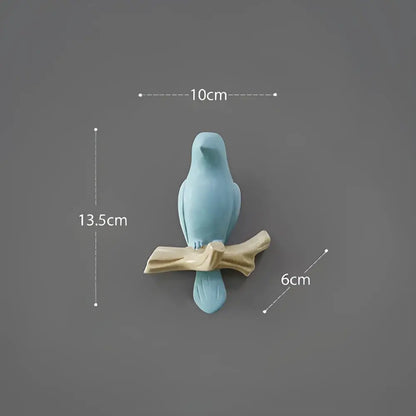A light blue ceramic decorbites bird resin hanger on a beige wood branch for wall decor and kitchen use