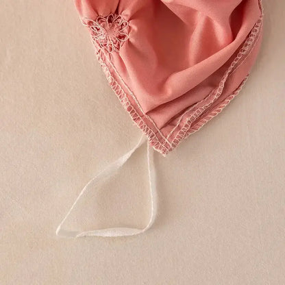 A delicate pink fabric bonnet with lace trim and white ribbon tie shown alongside a white diamond pinch pleated duvet cover set