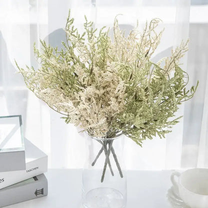 A delicate white dried baby’s breath lavender bouquet with green and cream foliage in a clear glass vase
