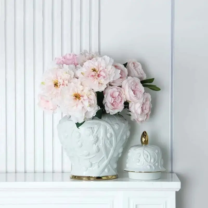 White embossed flower ceramic ginger jar vase with gold trim holding soft pink peonies for living room storage