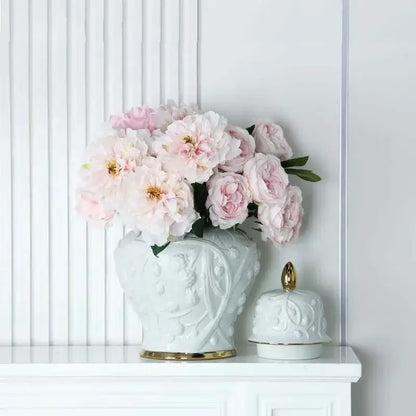 White embossed flower ceramic ginger jar vase with gold trim holding soft pink peonies for living room storage