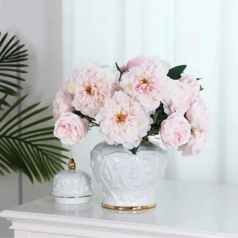 A white embossed flower ceramic ginger jar vase with gold trim holding soft pink peonies for living room storage