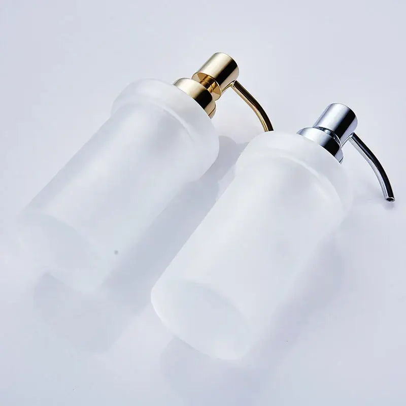 Two white frosted glass liquid soap dispensers with gold and chrome metallic pump heads for bathroom use