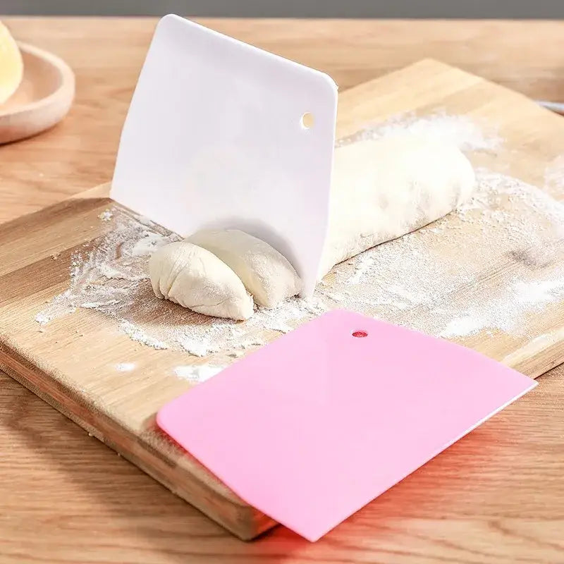 White and pink silicone cake cutter spatula set on wooden board for dough cream cake cutting and baking tasks