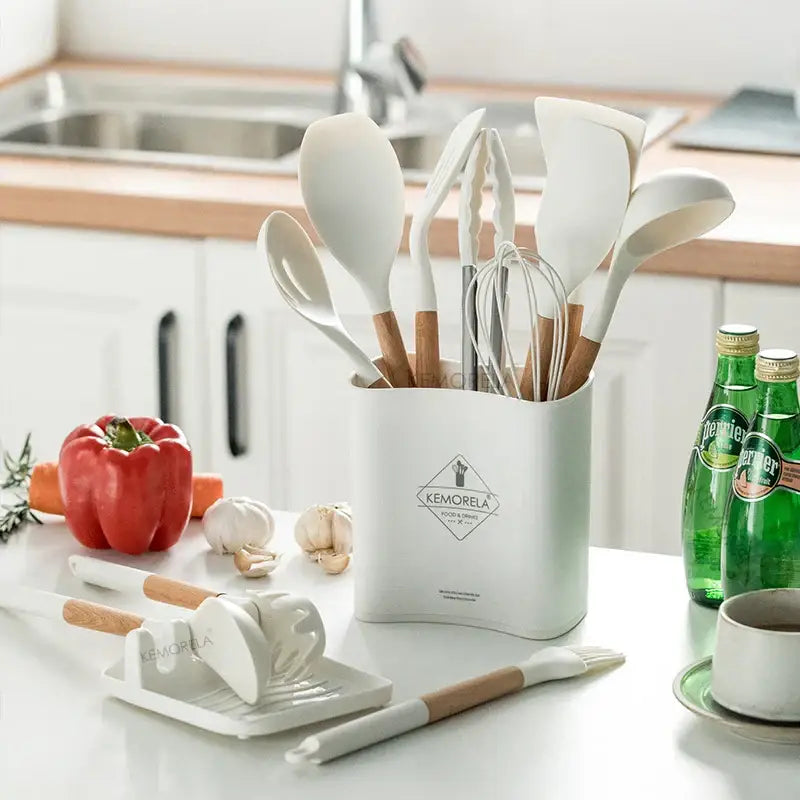 White silicone kitchen cookware set with wooden handles in a white ceramic utensil holder for kitchen organization