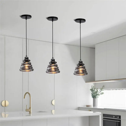 Three black decorbites iron cage pendant lights with spiral iron cage ring shades hang above a modern kitchen island