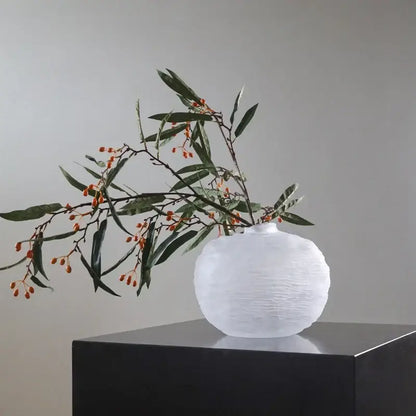 White textured ceramic glass pleats vase with rounded body and narrow neck holding green leaves and orange berries