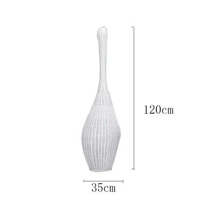 A tall slender white woven vase with flared top and tapered base next to a wicker dark brown bamboo floor lamp decorbites