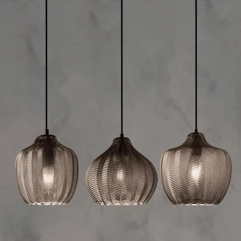 Three woven gold glass pendant lights with textured translucent chevron shades and dark metal frames for kitchen and dining