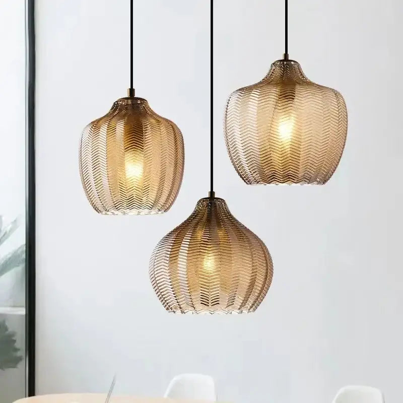 Three amber woven gold glass pendant lights with chevron texture hang from black cords ideal for kitchen and dining room