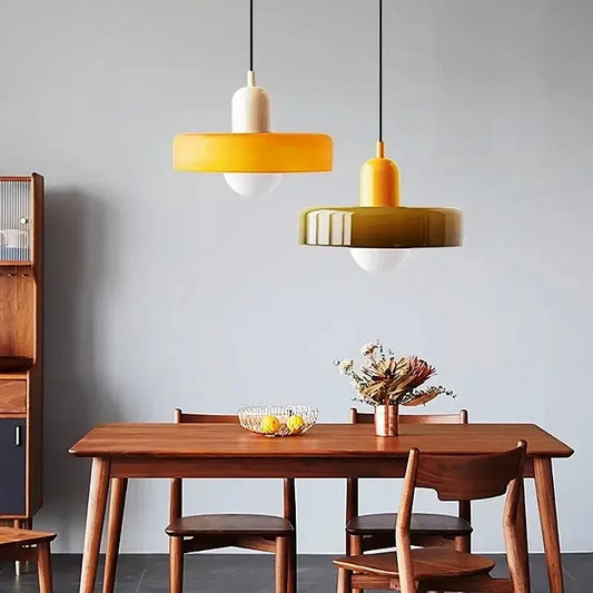 Two modern pendant lights with yellow and olive green colorful glass shades hang above a wooden dining table