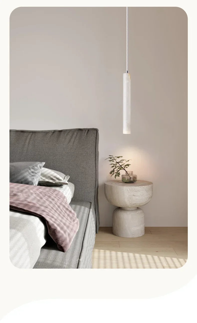 Minimalist white stone pendant light with sleek cylindrical design hanging above bedside table in bedroom