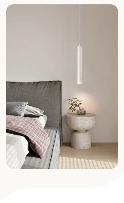 Minimalist white stone pendant light with sleek cylindrical design hanging above bedside table in bedroom