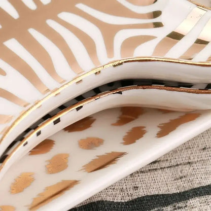 A white ceramic jewelry holder tray with gold tiger skin zebra stripe and feather motifs edged in shiny gold trim